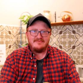 Young man with a beard wearing a red flannel shirt and a ball cap.